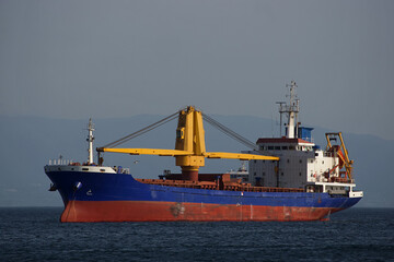 A vessel is anchored in a sea bay with a yellow industrial crane on board.