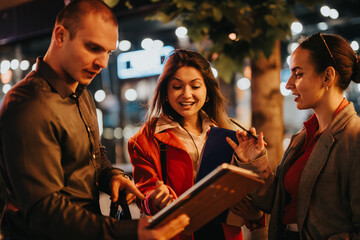 Three young corporate business partners collaborating and sharing ideas during an evening meeting outdoors, looking focused and engaged.