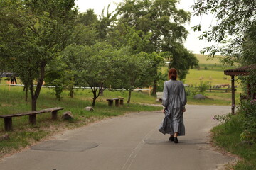 Fototapeta premium Young woman in old fashioned dress walking by the road from back