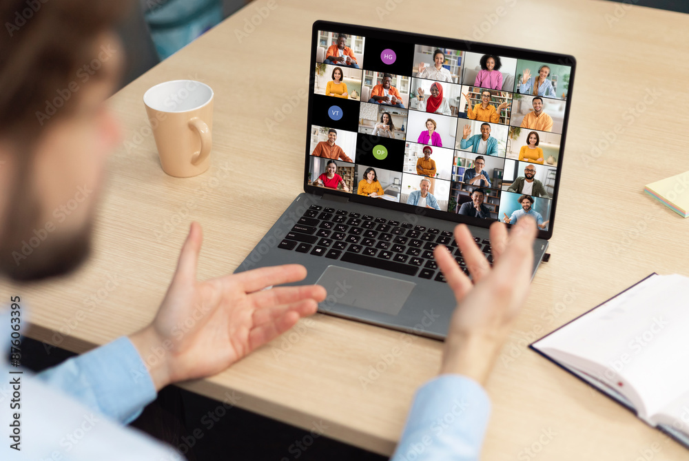 Poster a man sits at a desk in front of a laptop, actively participating in a video conference meeting with