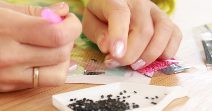 A close-up of a hand placing crystals on a canvas for a diamond painting 