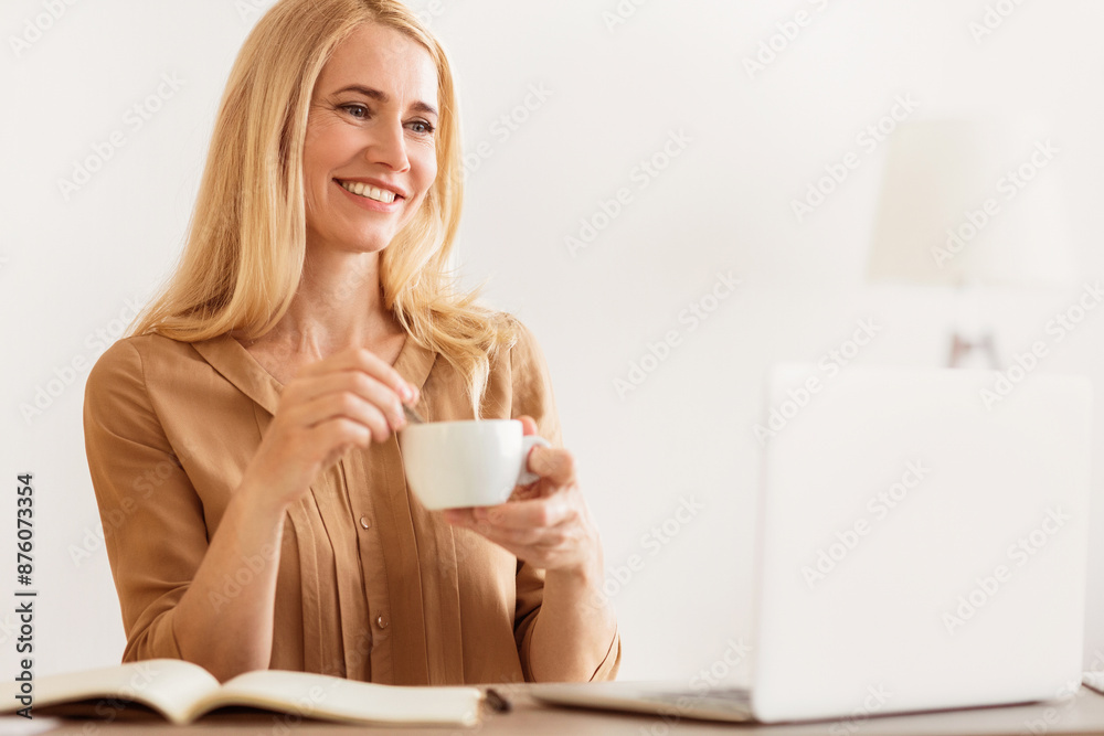 Poster a woman sits at a desk with a laptop and an open notebook, smiling as she enjoys a cup of coffee.