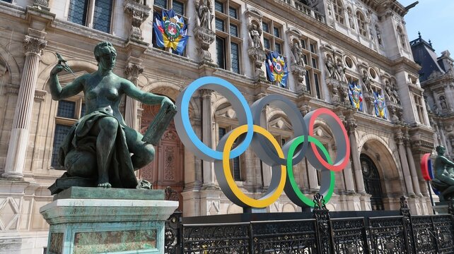 Anneaux olympiques, logo symbole des Jeux olympiques, devant la fa&ccedil;ade de l&rsquo;h&ocirc;tel de ville / mairie de Paris, pour les JO d&rsquo;&eacute;t&eacute; de Paris 2024, avec une statue &ndash;  mai 2023 (France)