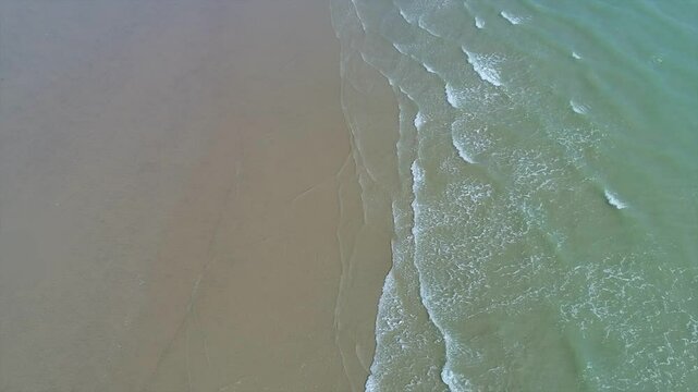 looking down at the surf on a sandy beach as gentle waves break on the shore