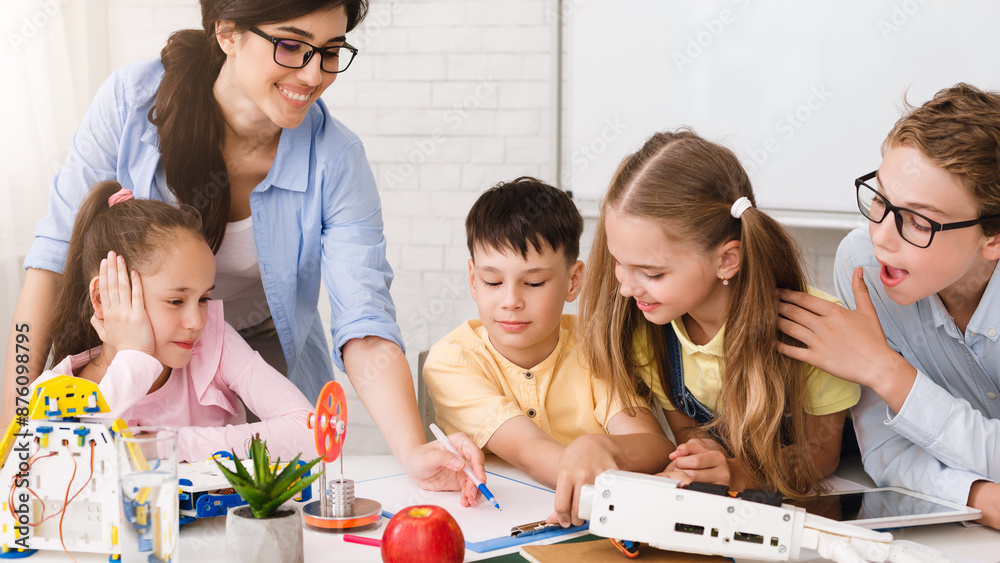Poster A group of elementary school students are engaged in a STEM learning activity in a classroom setting. They are working with robots and building models, and a teacher is guiding their learning