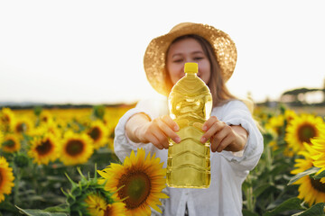 Female Farmer Holding A Bottle Of Sunflower Oil Against A Background Of Sunflowers. The Concept Of...