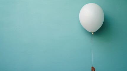 Minimalistic Image of a White Balloon Against a Turquoise Background with a Hand Holding the String