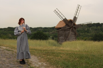 Beautiful brunette woman in vintage dress walking by brick road near old wooden windmill