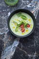 Bowl of chilled cucumber and green basil soup, flat lay on a black marble background, vertical shot, copy space