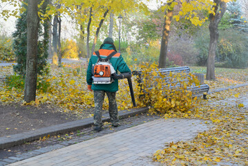 Cleaning up a city square from fallen autumn leaves with backpack leaf blower.