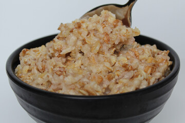 Cooked plain rolled oat inside black bowl and one silver spoon, Isolated on white background