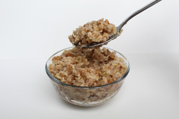 Scooping cooked rolled oats from a transparent glass bowl, isolated on white background