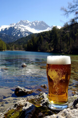 Leckeres goldenes bayerisches Bier mit Schaum in einem Glas neben einem See in den Alpen Bergen im Sommer