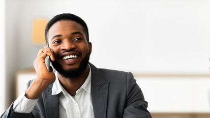 Pleasant conversation. Happy black businessman talking on cellphone at office, looking aside. Copy space