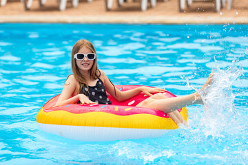 Pool party. Positive European teen girl float at swimming pool in pink sprinkled donut, festival, vacation, hotel, beach, event smiling with sunglasses, during summer, copy space. resort advertisement