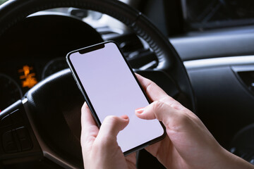 Woman sitting in a car and holding a smartphone with blank screen.