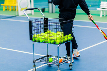 Tennis Coach Conducting Training Session with Tennis Trolley Nearby. A tennis coach conducts a...