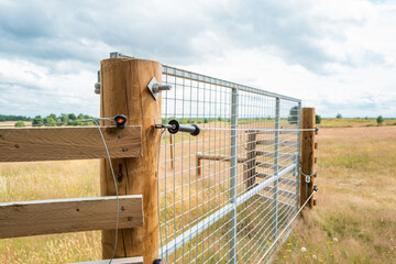 Newly erected farm field gate showing part of an electric fence which runs the perimeter of the large field, seen in rural Britain. © Nick Beer