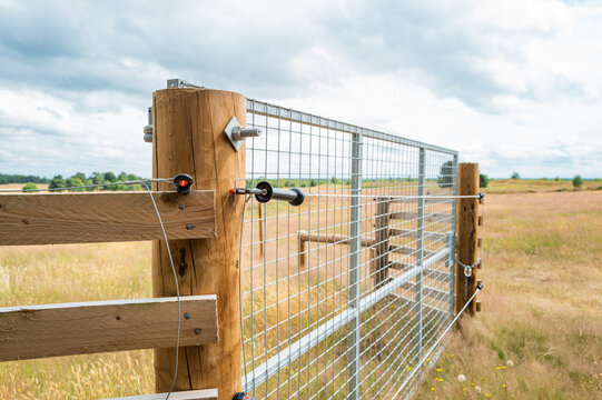 Newly erected farm field gate showing part of an electric fence which runs the perimeter of the large field, seen in rural Britain.
