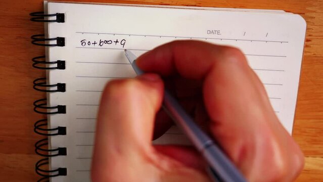A close-up photo of a hand holding a pen and writing on notebook in top view