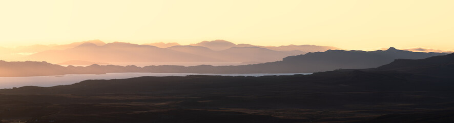 Panoramic view of hazy golden morning light breaking over mountains in The Scottish Highlands, UK.