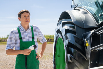 Farmer in green uniform stands next to electric tractor and holds electric vehicle charging plug