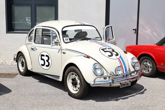 Azzida, Italy. July, 6 2024. Convertible white Volkswagen Type 1 , known as beetle and painted as Herbie of the film Love Bug, during a classic car rally. Open doors, side and front view.