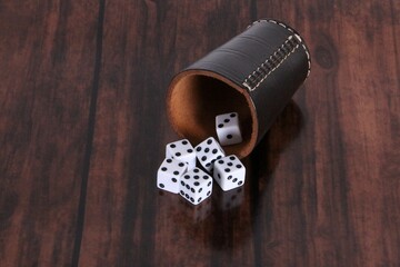 Leather dice cup lies on the wooden table and six white dice fall out
