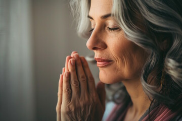 Middle-aged white woman with gray hair praying, hands clasped, eyes closed, conveying peace and introspection, concept of faith and meditation, includes Thanksgiving