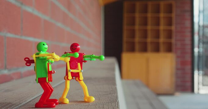 Video of two funny plastic windup toy dancing robots in a baseball softball dugout with a red brick wall. 
