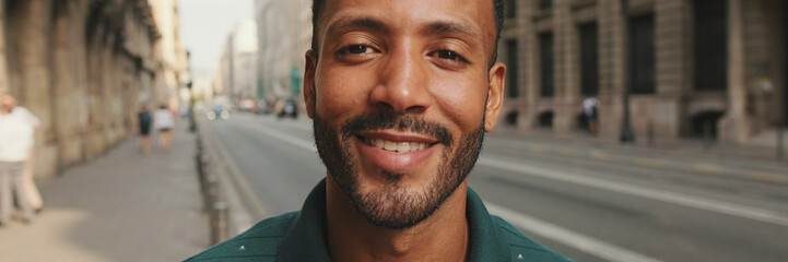 Fototapeta premium Close-up of happy young man standing on the street. Guy turns his head and smiles at the camera