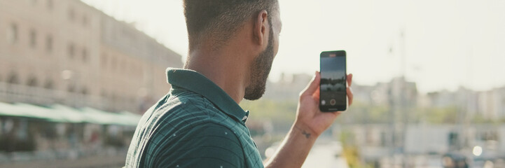 Young man takes photo on smartphone yachts in the seaport.