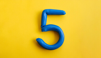 Naklejka premium Numbers 5 made of blue plasticine on yellow background. Math learning, development. Flat lay