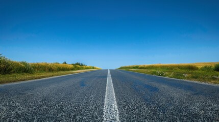 Naklejka premium a straight gray asphalt road, blue vibrant clear sky.