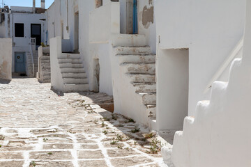 Quiet street in Antiparos, Greece, featuring traditional whitewashed buildings with rustic stairs and a cobblestone path. This serene scene captures the essence of Cycladic architecture and charm.