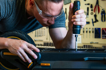 Repairing an electric scooter in a workshop. A close-up shot of a master disassembling a scooter with an electric screwdriver. © Konstantin