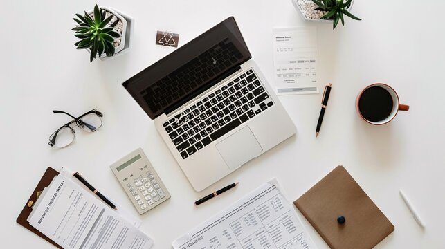 An overhead shot of a minimalist workspace with a laptop, financial statements, a calculator, a pen, and a cup of coffee on a white desk.