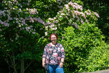 A woman wearing glasses stands in front of a tree with pink flowers