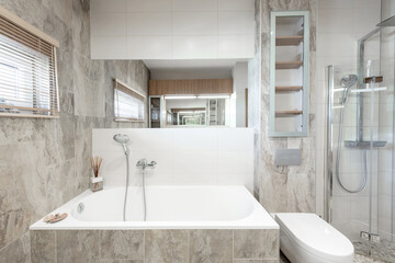 Bright Elegant Modern Bathroom Interior Design of Shower Room With White Bath. Bathroom Accessories, Gray Tile Walls, Mirror, Lavatory, Toilet. LED Light.