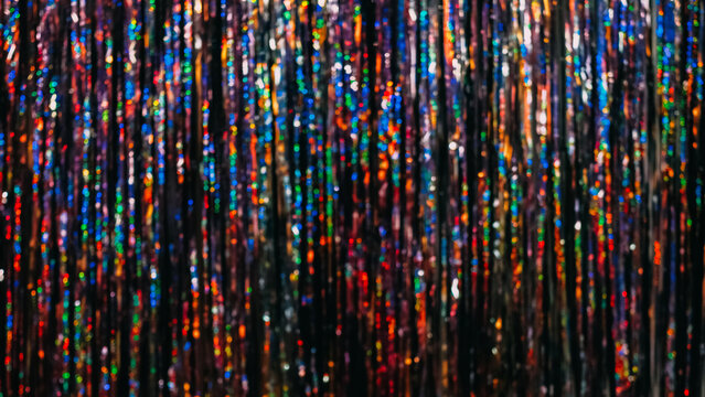 Festive tinsel texture. Bokeh light. Holiday party decor. Defocused red purple blue green orange neon color rainbow curtain glow sparkle blur circles pattern abstract background.