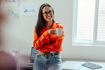 Woman in orange shirt holding coffee cup and smiling in a bright office environment