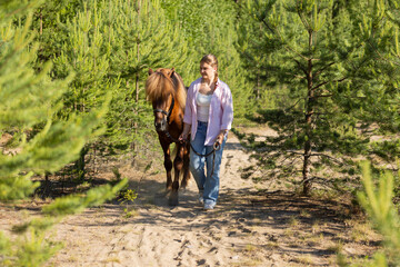 Fototapeta premium Woman with Icelandic horse between pines at summer evening