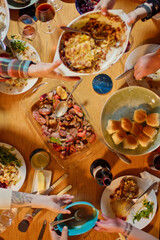 4K Ultra HD image of Top Down Shot of People Gathered Around Dining Table for Friendsgiving Party Passing Plates of Food