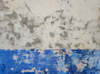 Close-up of an old wall with weathered paint and peeling layers. White and blue old wall with peeling paint