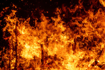 A dramatic image of a fierce fire burning intensely against the dark night sky. The bright orange...
