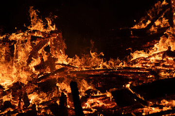 A dramatic image of a fierce fire burning intensely against the dark night sky. The bright orange and yellow flames highlight the raw energy and destructive power of the blaze. Copy space available.