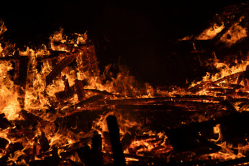 A dramatic image of a fierce fire burning intensely against the dark night sky. The bright orange and yellow flames highlight the raw energy and destructive power of the blaze. Copy space available.