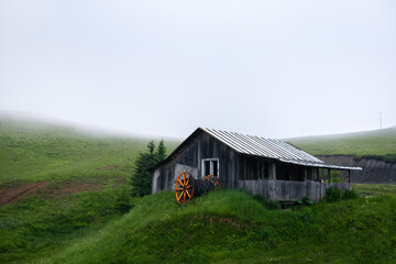 Abandoned wooden house on the green hills in foggy day. Natural landscape.