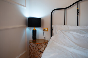 Interior of bedroom with white blanket on bed and black lamp on golden bedside table.