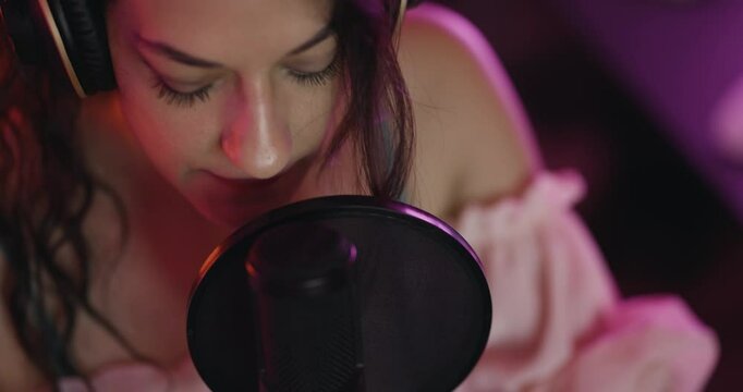 Female music producer in studio with audio recording equipment. Girl snging on a professional studio microphone. Close up abstract video.